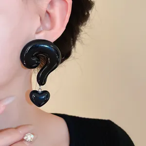 Detailed close-up of retro glossy black question mark earrings with a heart charm