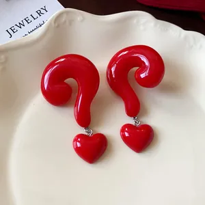 Detail of glossy red question mark earrings with heart charms on a ceramic plate.