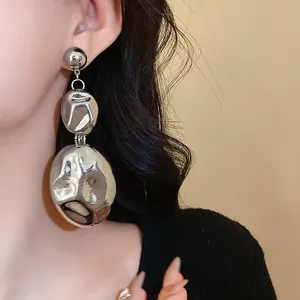 Close-up detail of oversized silver crinkled metal drop earrings on a model's ear