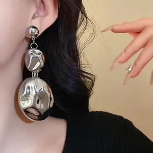 Close-up detail of oversized chunky irregular metallic silver drop earrings on a model