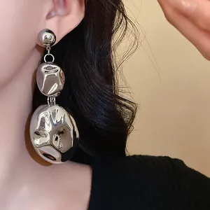 Detail of oversized silver crumpled metallic tiered dangle earrings on model