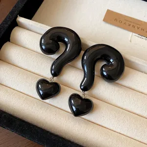 Close-up view of glossy black question mark earrings with heart dangles in a display box.