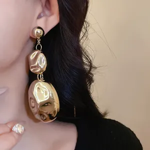 Close-up of oversized gold textured metal drop earrings worn by a model