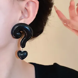 Close-up detail of glossy black question mark earrings with a heart dangle pendant