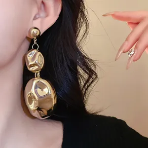 Detail of chunky gold crinkled oval earrings worn by a stylish model with dark hair.