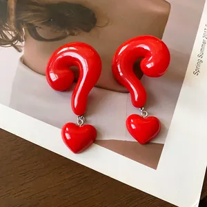 Detailed close-up of unique red question mark and heart drop earrings with high-gloss finish