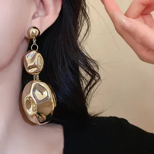 Close-up of oversized gold oval dangle earrings with wrinkled texture on model