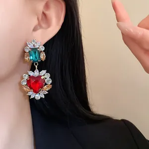Macro degli orecchini a cuore vintage con zirconi smeraldo e rossi sulla modella.