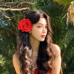 Close-up of a large red rose hair clip worn by a model in a tropical outdoor setting.