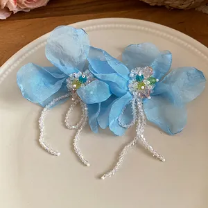 Macro detail of elegant light blue chiffon flower earrings with sparkling bead tassels