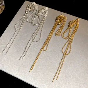 Close-up detail of 18k gold and silver plated long ball chain tassel ear clips in vintage style