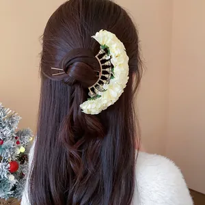 Crescent-shaped white fabric flower hairpin worn on a brown hair bun detail view