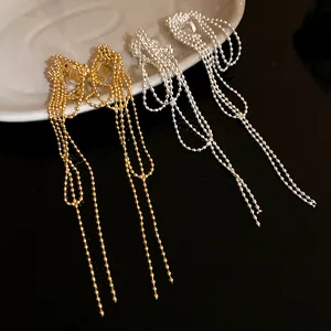 Detail of gold and silver knotted bead chain tassel clip-on earrings on a white plate.