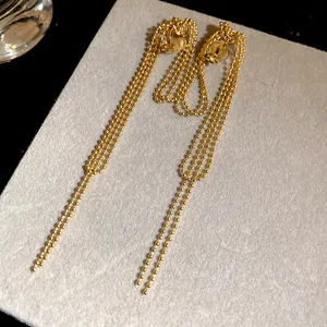 Close-up of 18k gold plated bead chain tassel ear clips on a gray display card
