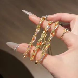 Détail de trois élégants bracelets en zircon colorés et torsadés tenus dans une main