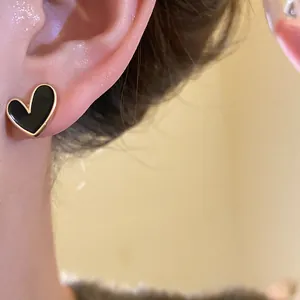 Close-up shot of elegant black heart-shaped stud earring worn on ear with gold trim finish