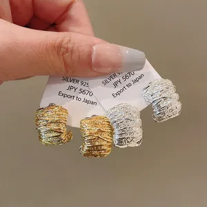 Dettaglio macro di orecchini a cerchio geometrici a pieghe in finiture oro e argento.