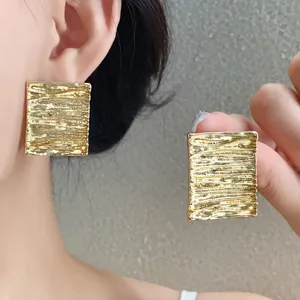 Close-up of golden square stud earrings with unique crumpled metallic texture design