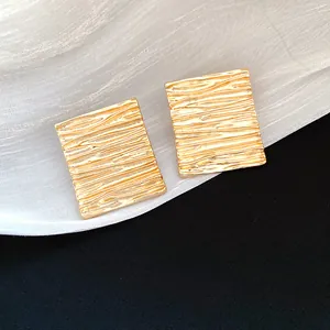 Close-up of gold rectangular earrings with elegant ripple texture finish