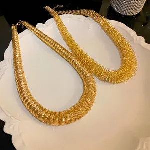 Elegant gold oversized spring cut statement necklace displayed on a white plate