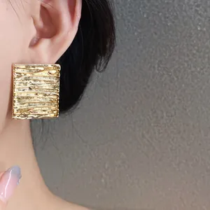 Close-up detail shot of gold-finished wrinkled square stud earrings on an Asian model.