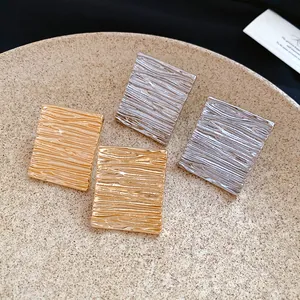 Close-up of gold and silver rectangular wrinkled earrings on a textured beige plate.