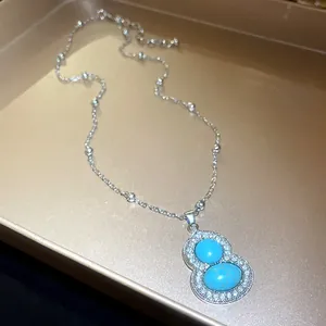 Detail of a silver gourd necklace with turquoise stones and rhinestone paving on a tray.
