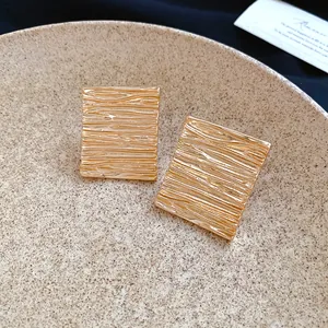 Macro view of gold-plated geometric stud earrings featuring a unique wrinkled texture