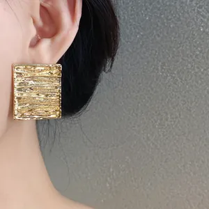 Close-up detail of gold square stud earrings with wrinkled texture on model's ear