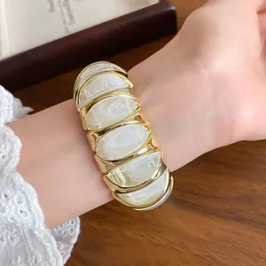 French style marbled acrylic geometric bracelet on wrist, elegant gold and white jewelry.