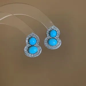 Close-up of silver-toned gourd earrings with turquoise stones and pave diamonds