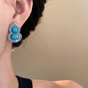 Close-up of elegant gourd-shaped silver earring with turquoise stones worn by a model