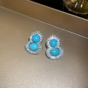 Close-up of gourd-shaped silver stud earrings with pavé diamonds and turquoise stones.