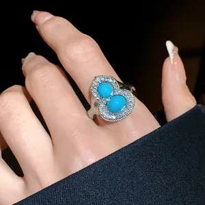 Close-up of an elegant silver ring with two turquoise stones and a diamond-encrusted frame