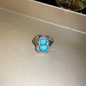 Close-up view of a gourd-shaped ring with turquoise stones and sparkling diamonds.