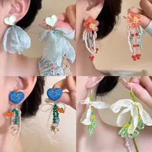 Dettaglio di orecchini colorati a fiore con nappe e ago in argento dolce.