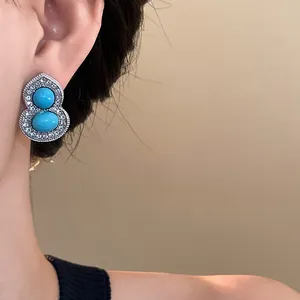 Close-up of gourd-shaped stud earrings with turquoise stones and pavé crystals on ear.