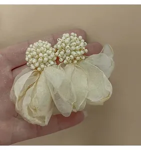 Primo piano di eleganti orecchini a fiore in perline beige e tessuto organza in mano