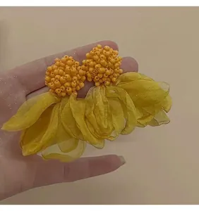 Dettaglio di orecchini a fiore gialli con petali in rete a strati e decorazioni di perline