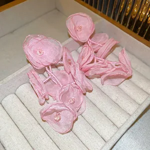 Dettaglio di orecchini pendenti con fiori in organza rosa e steli di perline delicate