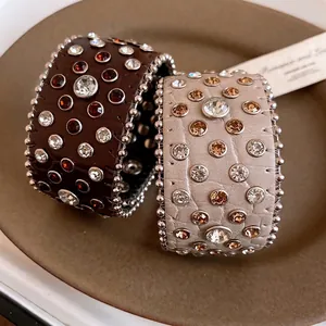 Bracciali vintage in pelle con strass colorati e borchie presentati su un piatto di ceramica.