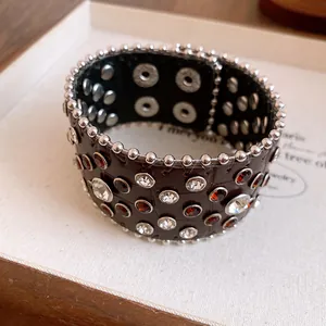 Dettaglio ravvicinato di un bracciale in pelle vintage con strass rossi e rivetti argentati