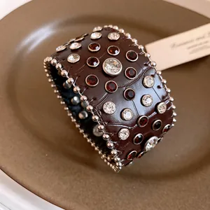 Dettaglio di un bracciale a fascia in pelle marrone coccodrillo con strass e borchie d'argento.