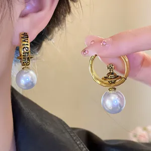 Close-up detail of retro Saturn orb pearl earrings with Vivienne lettering engrave