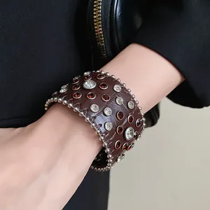 Vista dettagliata di un bracciale a polsino in pelle marrone con strass e borchie argentate.