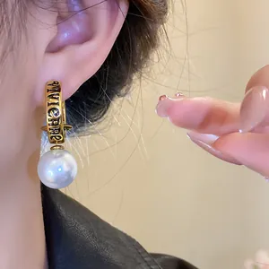 Close-up of a luxury retro Saturn earring with imitation pearl and engraved letters