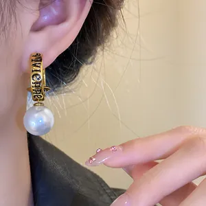 Close-up of retro gold hoop earring with VIVIENNE engraving and a large white pearl.