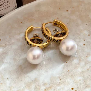 Close-up of retro Vivienne Saturn hoop earrings with faux shell pearls in a golden finish.