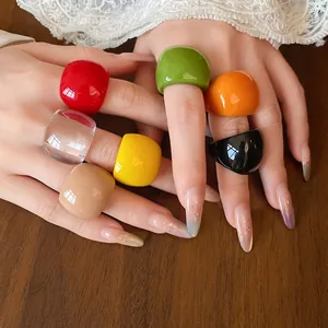 Dettaglio di anelli ovali in resina multicolore sulle dita con sfondo in pizzo