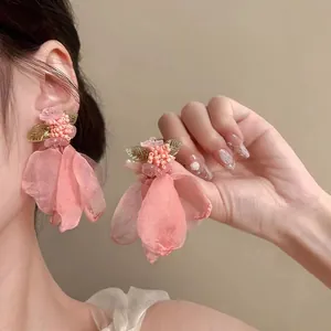 Dettaglio di orecchini a nappa con fiori in tessuto rosa e accenti di perline e foglie